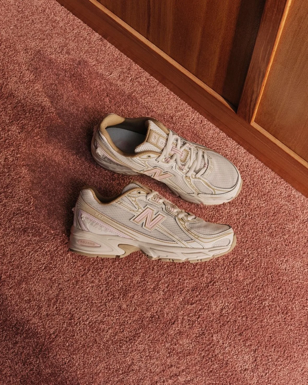 Top-down pair of cream and tan mesh sneakers with pink N logos on pink carpet, Sakura