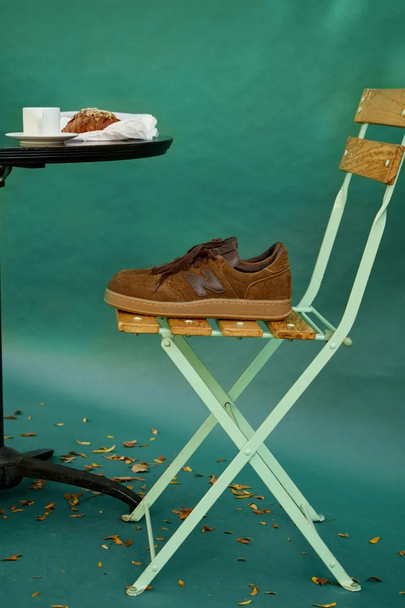 Lateral view of brown suede sneaker on a mint folding chair by a cafe table with croissant, Café