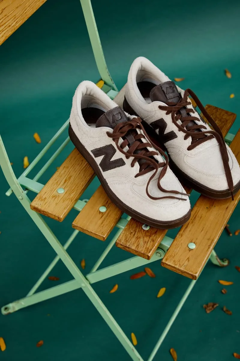 Pair of cream suede sneakers with brown N logos and laces on a mint green folding chair, Café