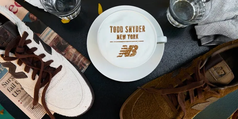 Top-down latte with Todd Snyder New York and logo in foam, cream and brown suede sneakers either side, Café