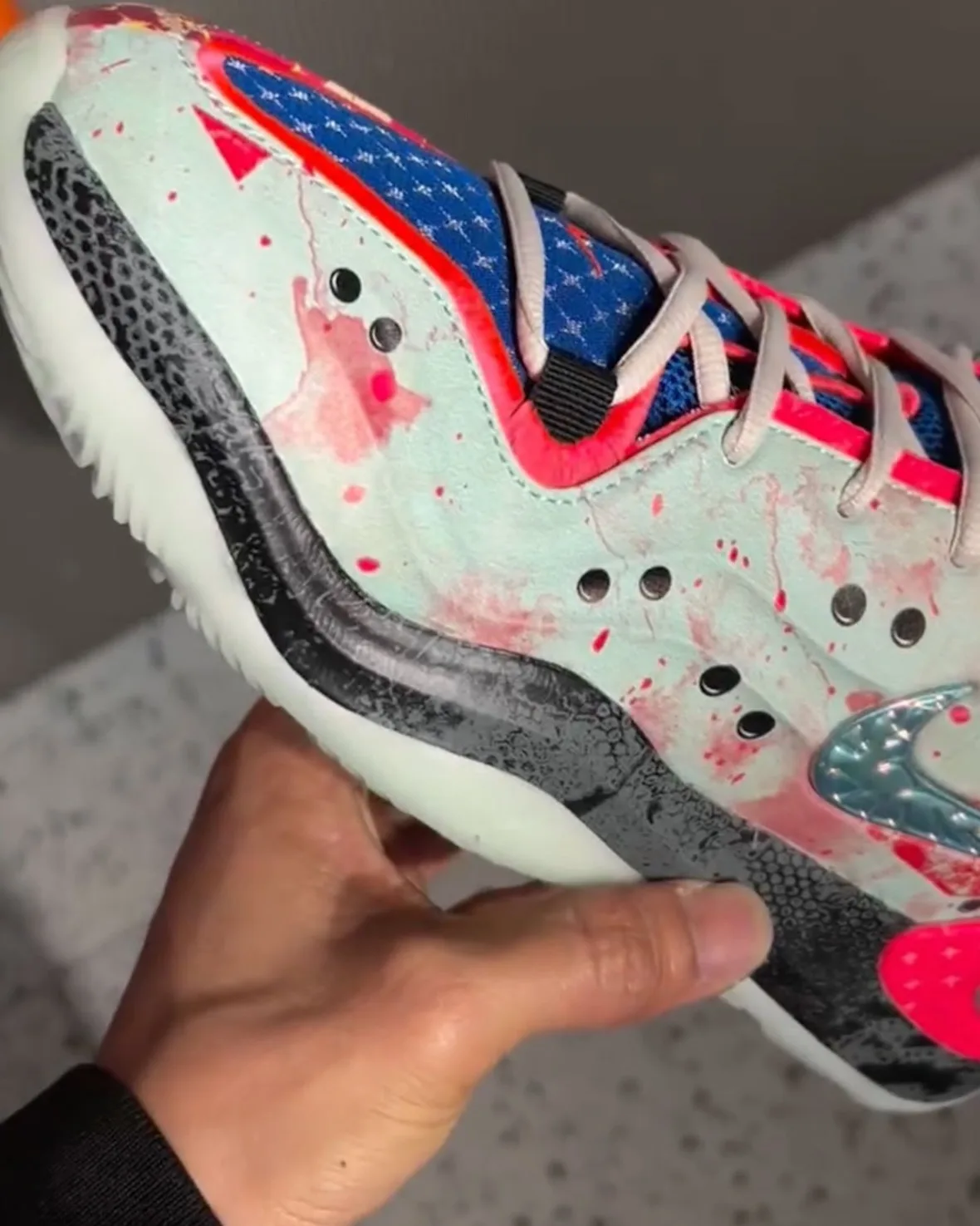 Lateral in-hand detail of pale mint upper with pink splatter, blue mesh tongue, grey laces and black speckled midsole band