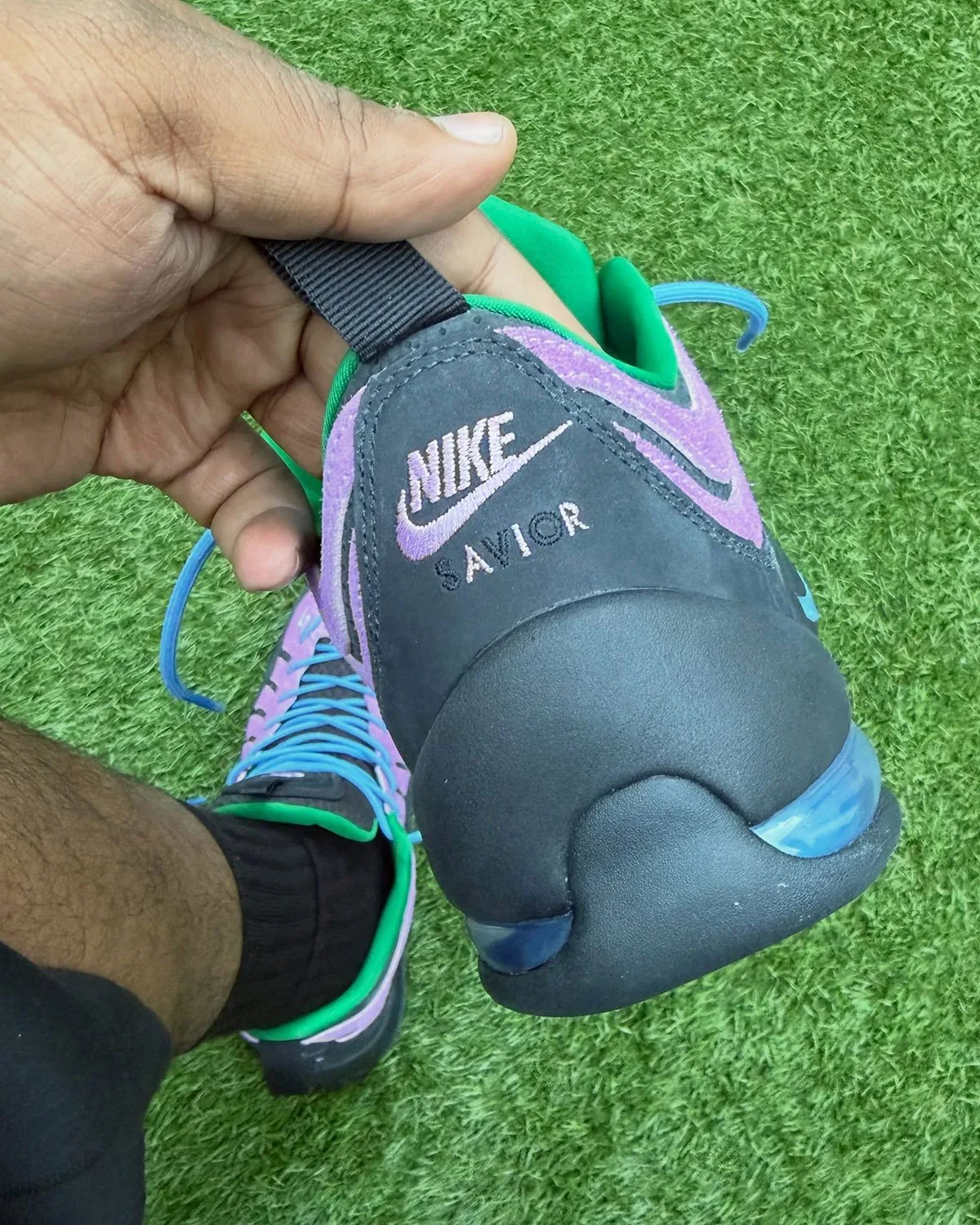 Heel view held in hand: Nike and Savior embroidery on black heel, blue air unit, Purple Stardust