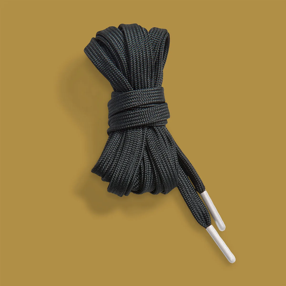 Coiled flat black shoelaces with white tips on mustard gold background, White/Black