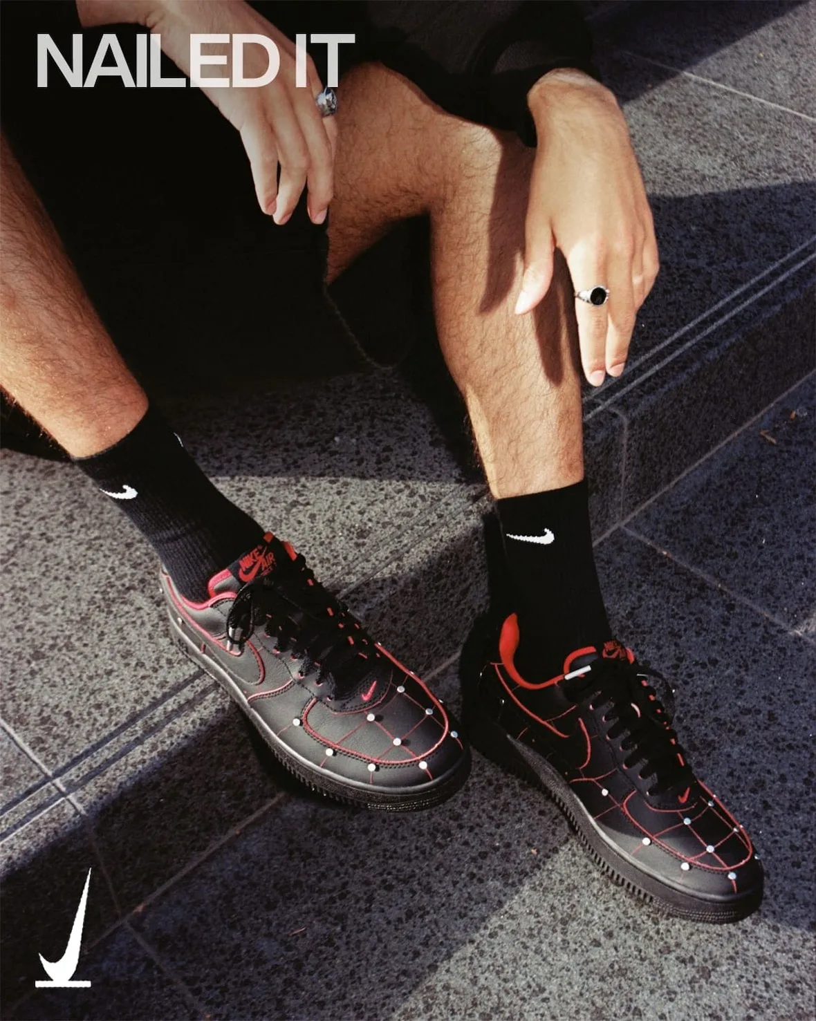 On-foot view seated on steps, black Nike socks, silver rings, black shoes with red grid lines and studs, Nightmare