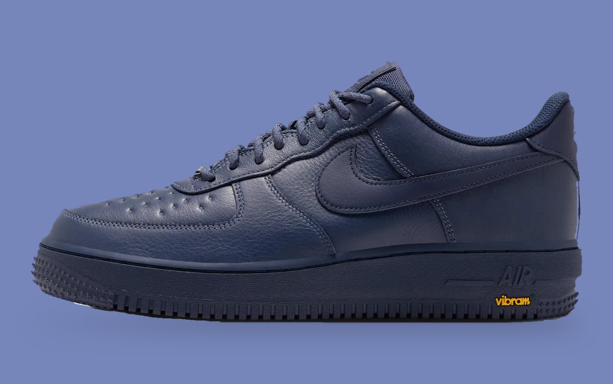 Lateral view of navy leather sneaker with tonal swoosh and Vibram logo on periwinkle, Thunder Blue