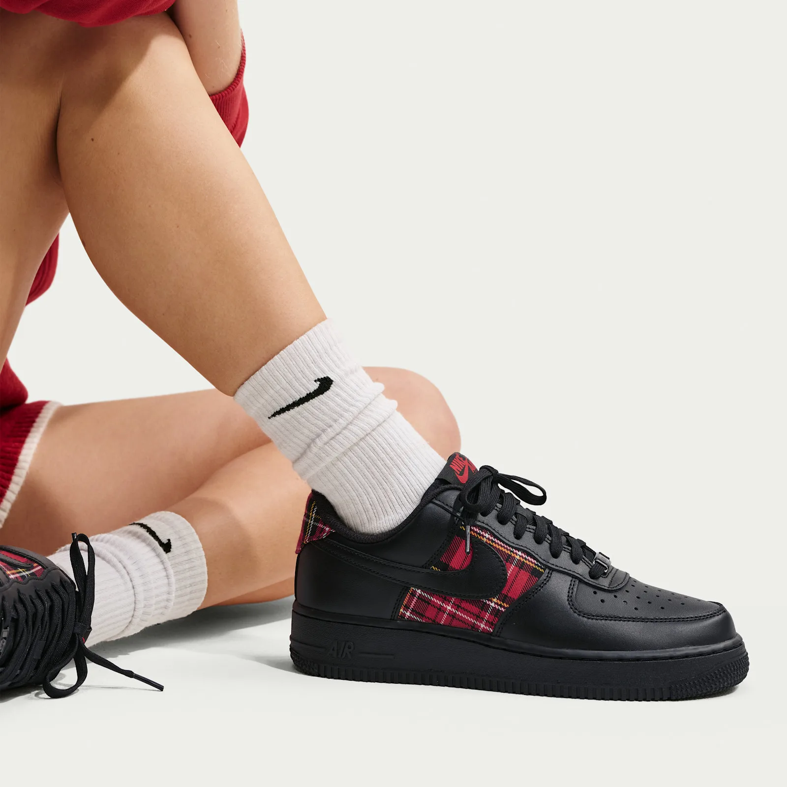 On-foot, seated model in white Nike crew socks and red clothing, black shoe with red plaid, Red Plaid