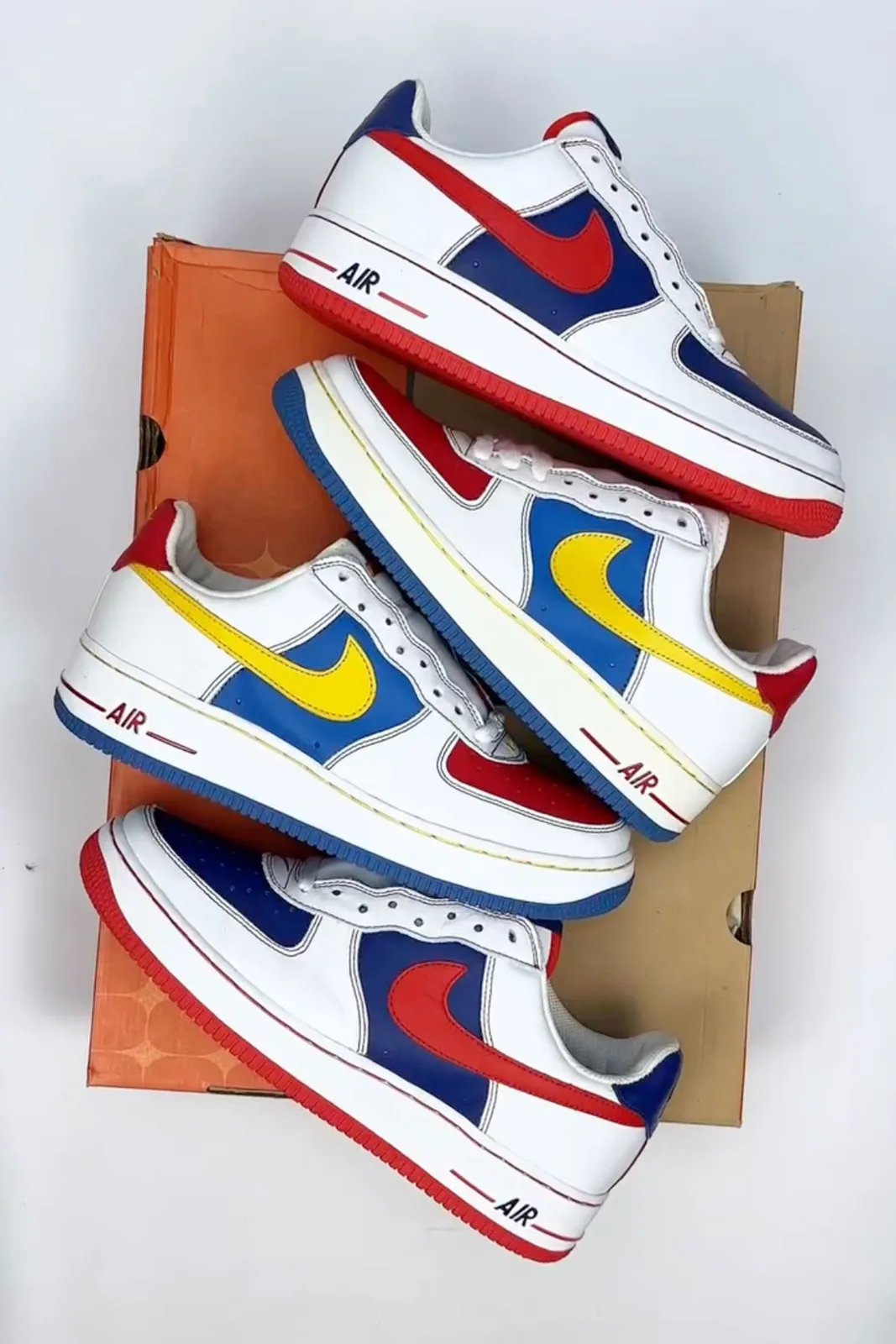 top-down pair stack on orange shoebox, red/blue/yellow colourways with white midsoles, Remix Da Kickz