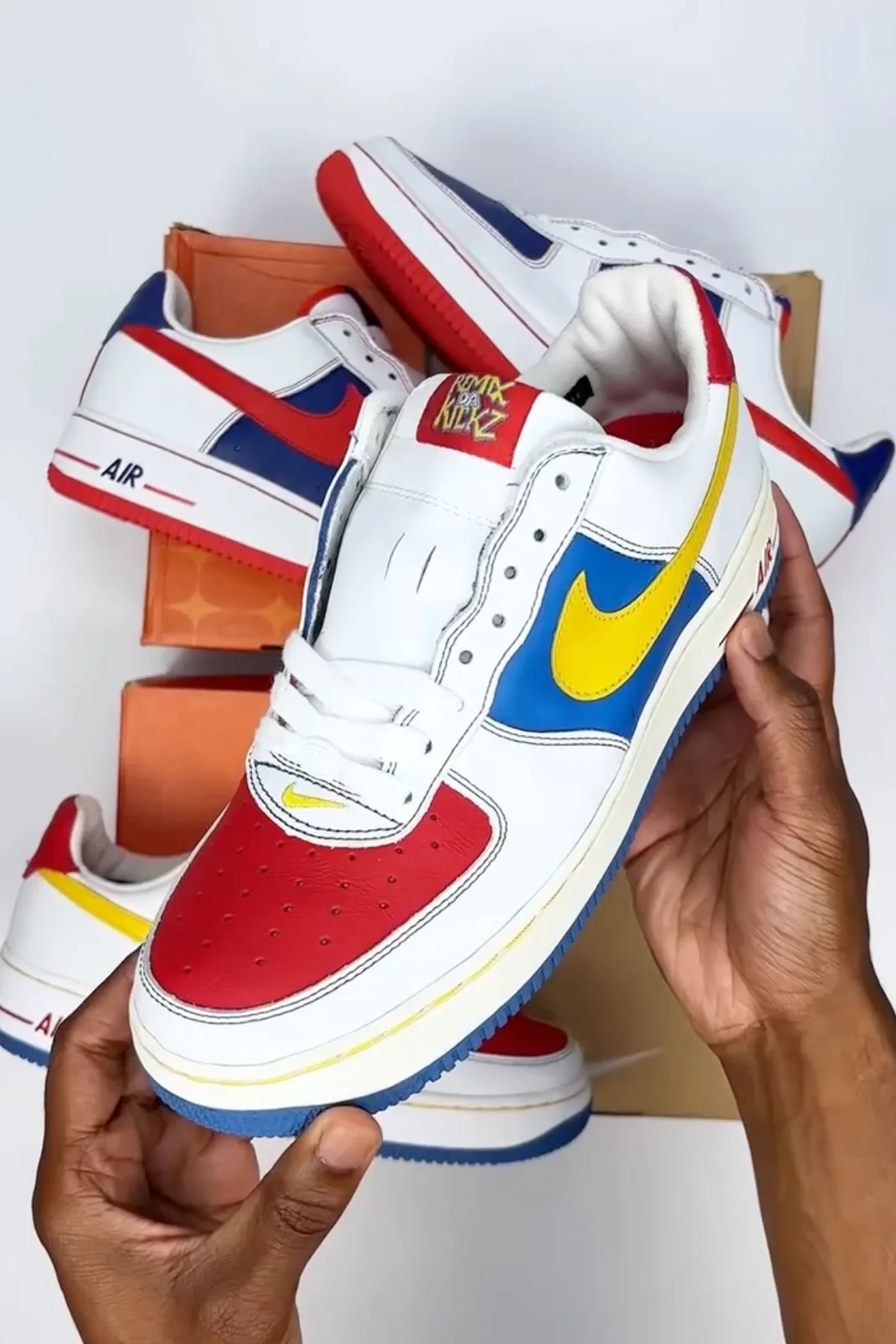 in-hand lateral view, white and blue with yellow swoosh, red remix da kickz tongue tag, Remix Da Kickz