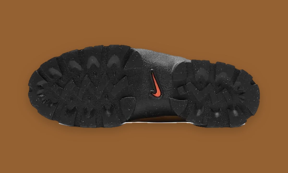 Outsole view with black lugged tread, speckled flecks and small orange swoosh, Black