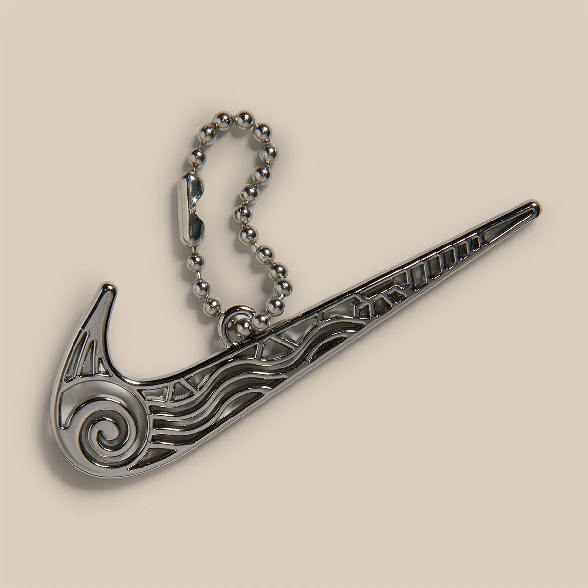 Silver metal Swoosh charm with spiral cutouts and ball chain on beige backdrop, Light Orewood Brown