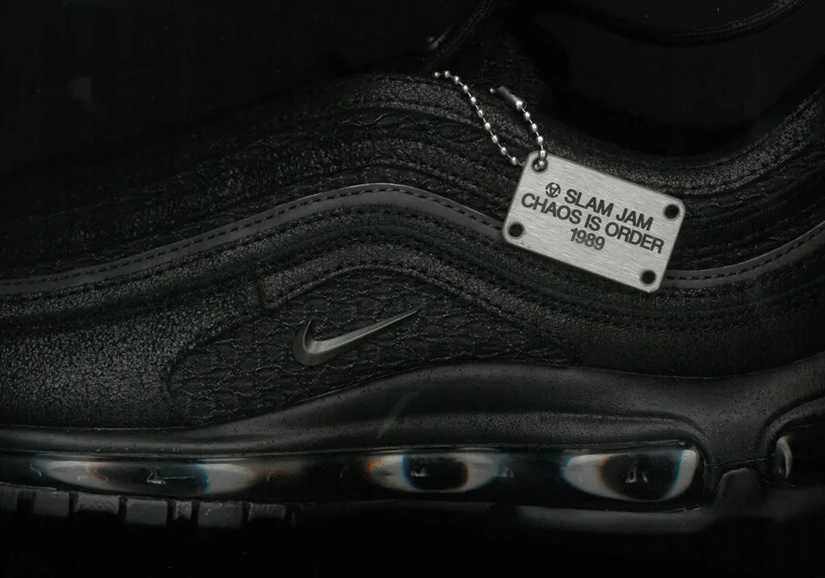 Close lateral detail of black textured upper, tonal swoosh and metal tag reading Chaos is Order 1989, Black