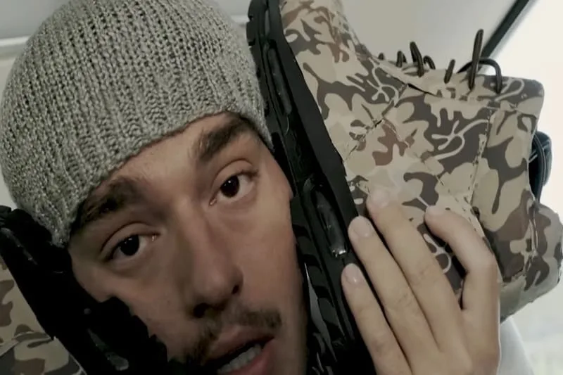 In-hand side view of camouflage boot with chunky black sole beside a face, Camo