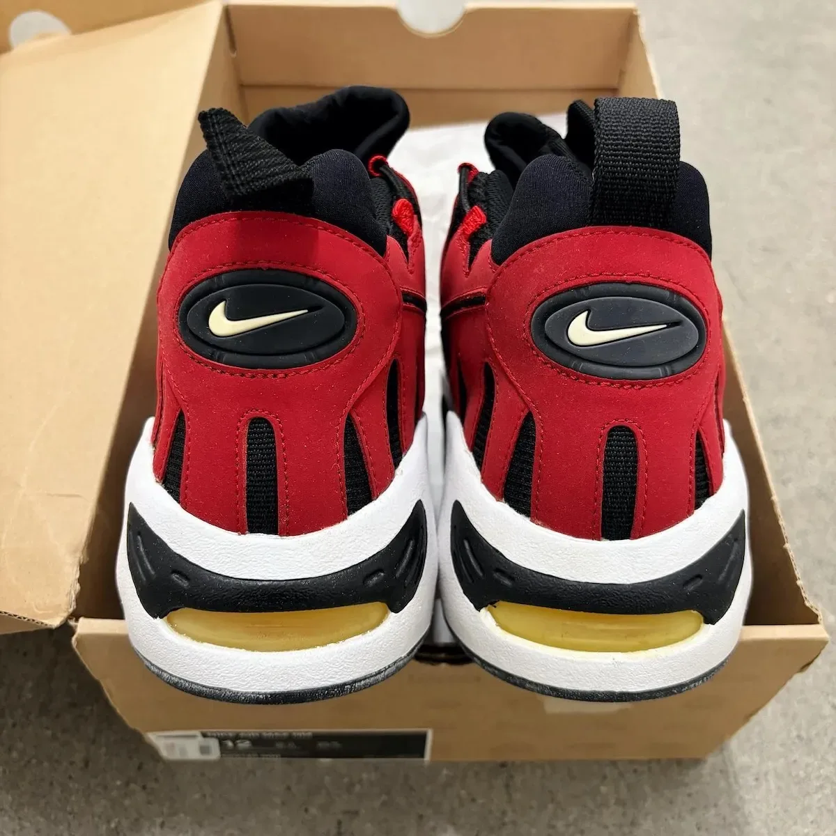 Heel view of pair in an open shoebox, black and red heels with cream swoosh, yellow air unit, Varsity Red