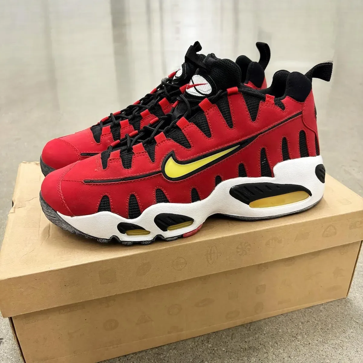 Lateral pair on a cardboard box, red suede, yellow swoosh, black laces, white midsole, Varsity Red