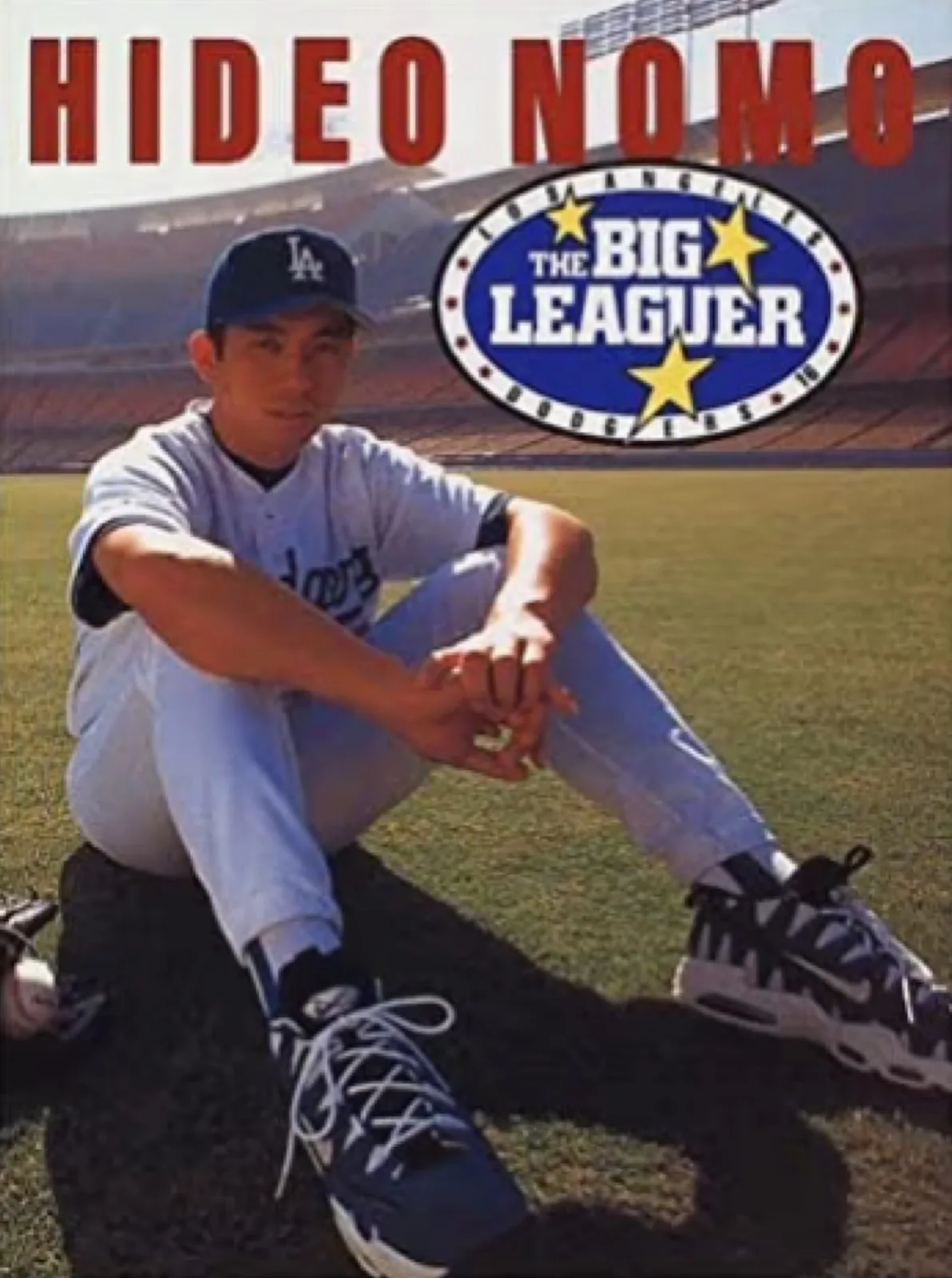 Player in Dodgers uniform sitting on grass, Hideo Nomo title and The Big Leaguer badge, Varsity Red