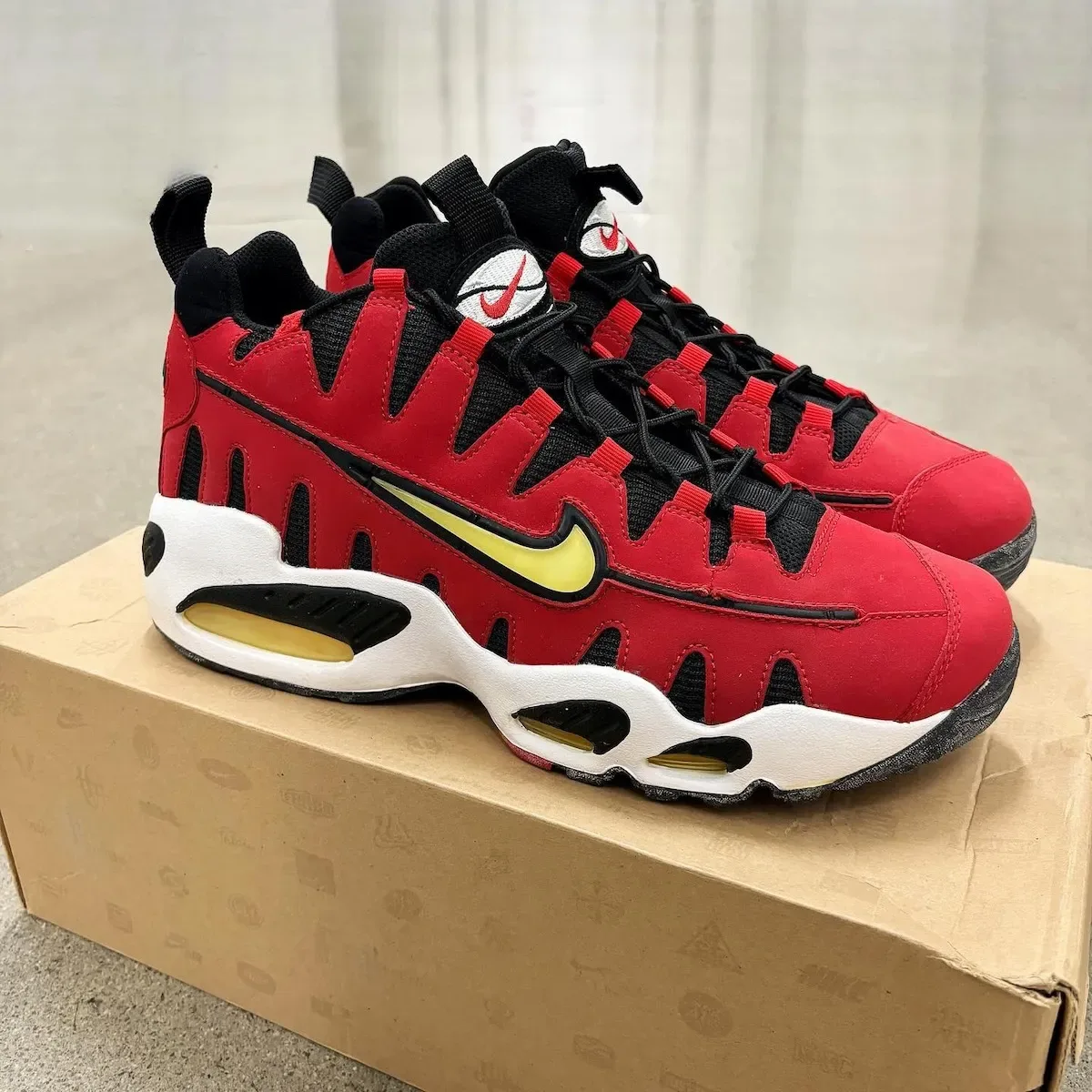 Lateral pair on a cardboard box, red upper, yellow swoosh, white midsole with black cutouts, Varsity Red