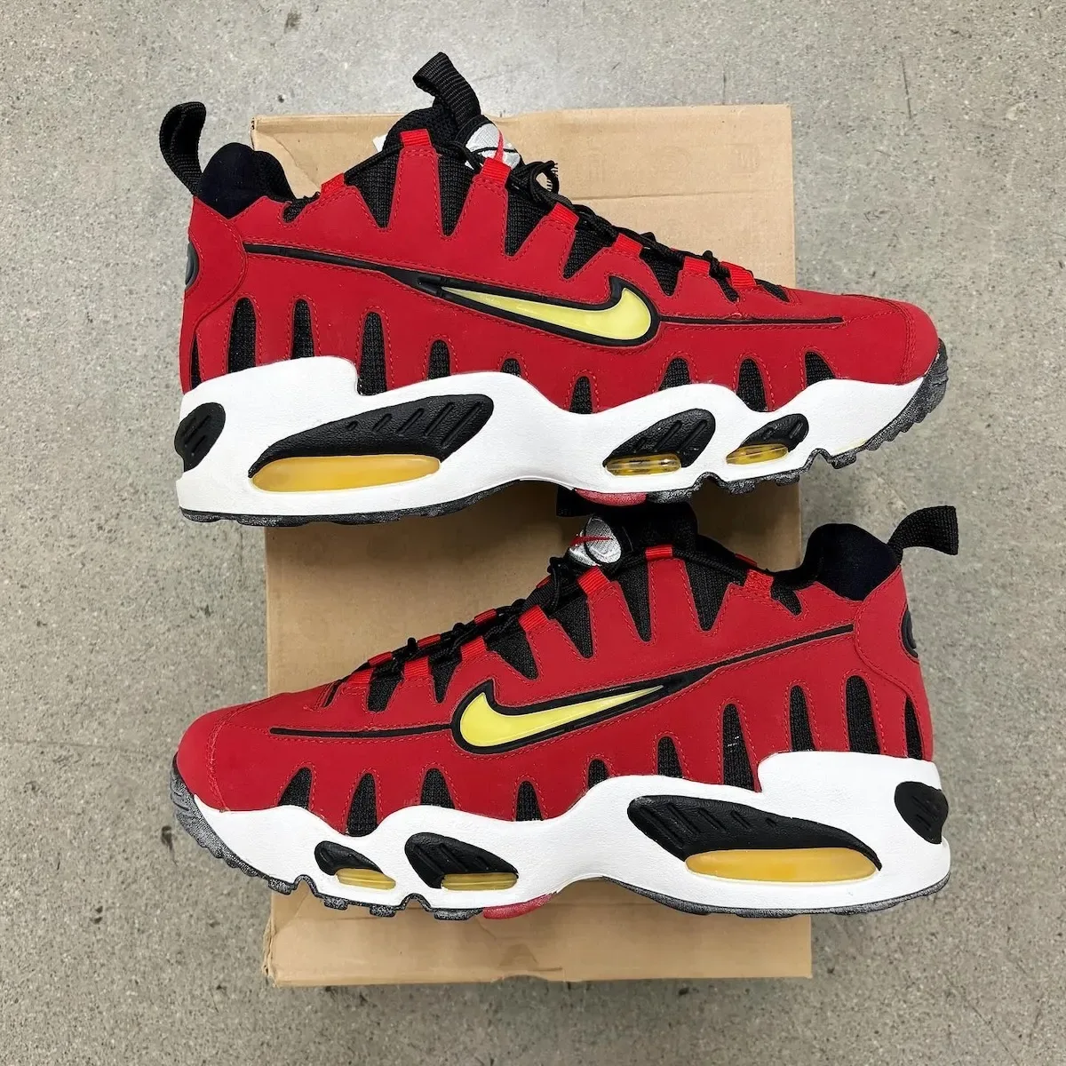 Top-down pair of lateral sides on a box, red and black upper, yellow swoosh, concrete floor, Varsity Red