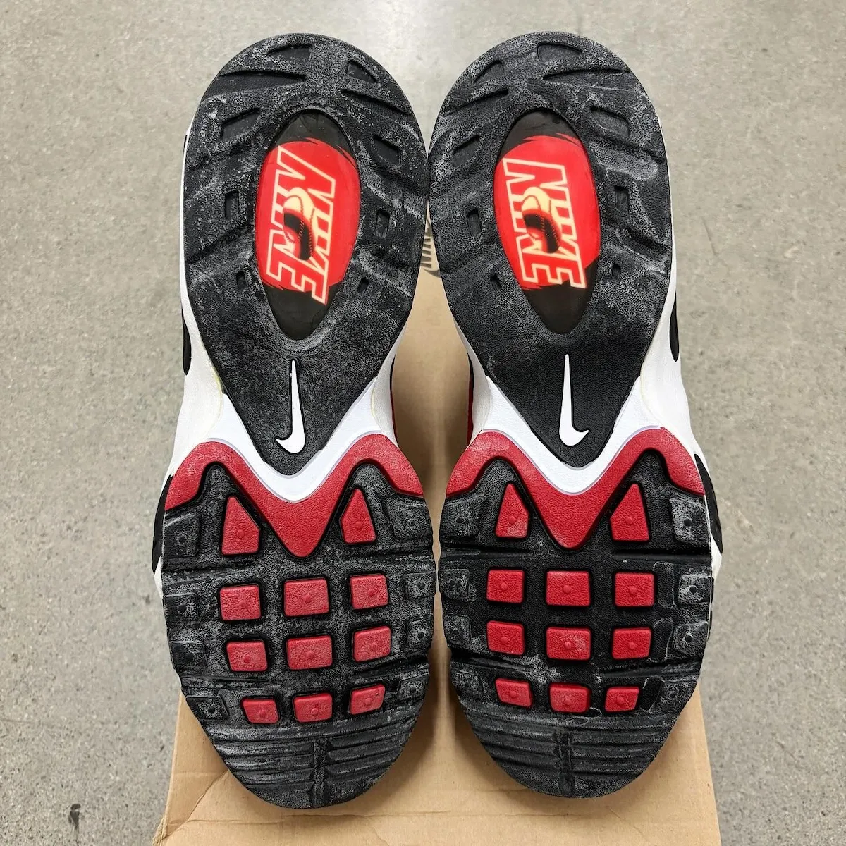 Outsole view of pair, black rubber with red pods, red Nike logo plug and white swoosh, Varsity Red