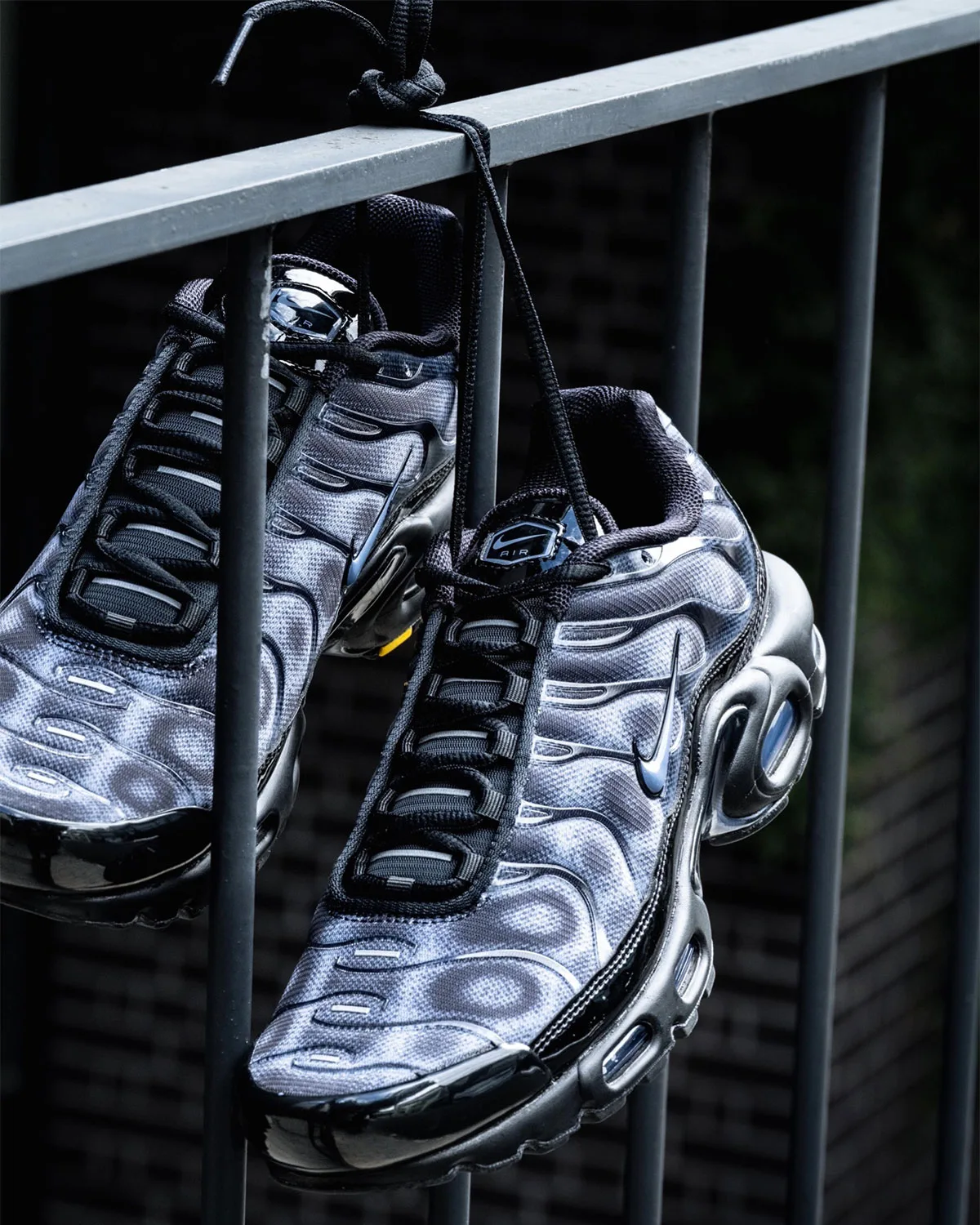 Pair hanging from railing by knotted black laces, top-down angle, blue-grey mesh, black patent toe, Black/Cool Grey