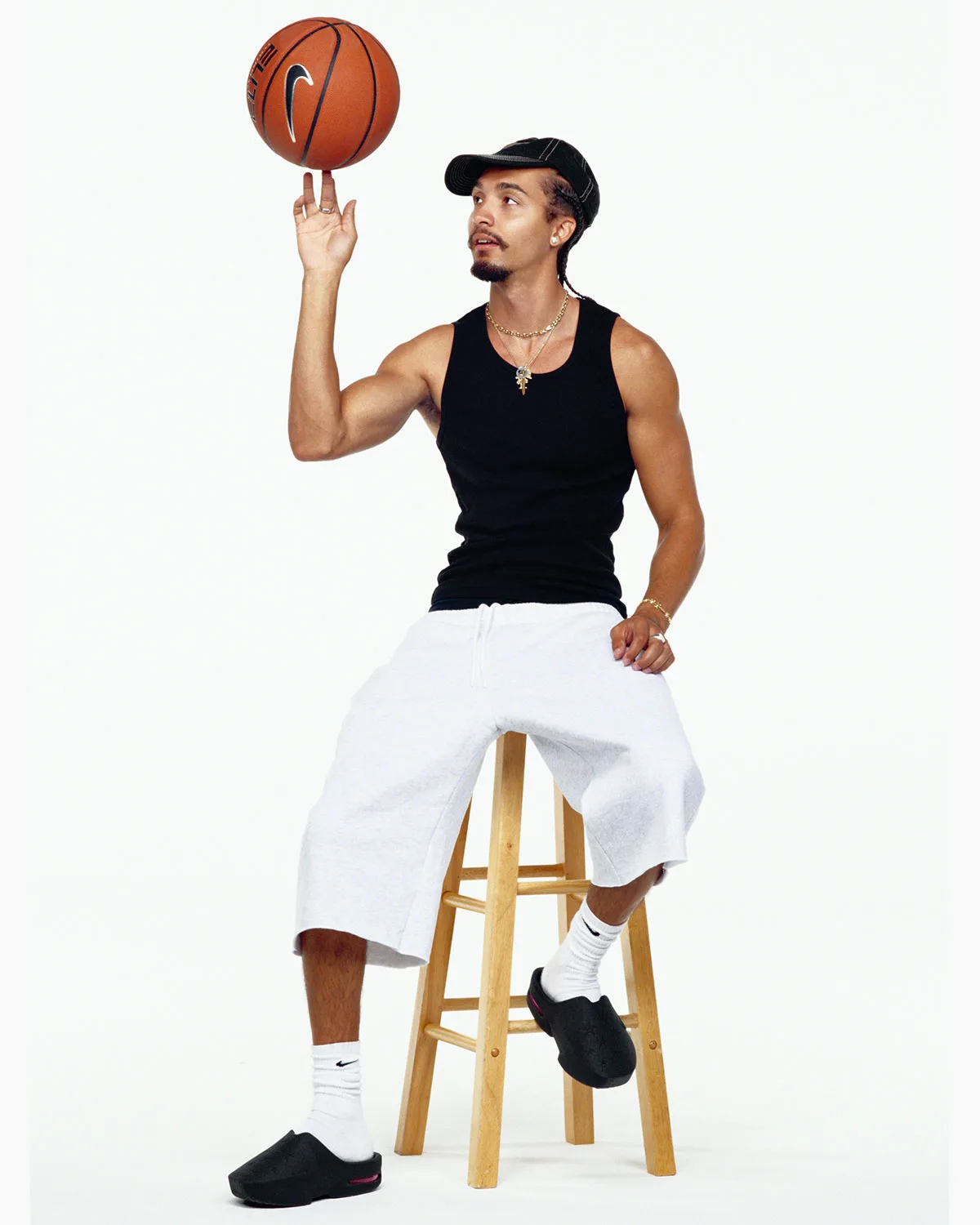 Person seated on a stool spinning a basketball, wearing black mules, white socks, grey shorts, Air Max Mule