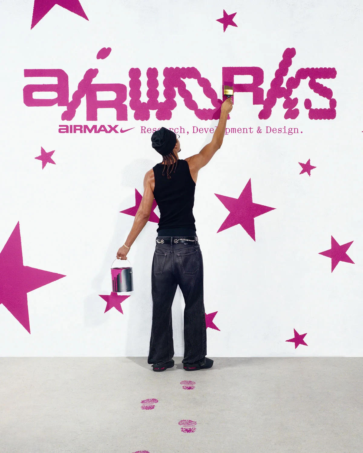 Person painting pink Air Works lettering and stars on a white wall, black mules seen from behind, Air Max Mule