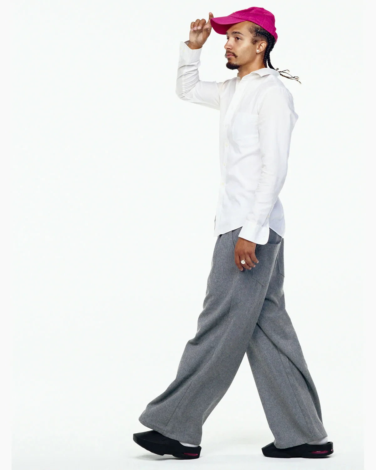 On-foot side view of person walking in pink cap, white shirt, wide grey trousers and black mules, Air Max Mule