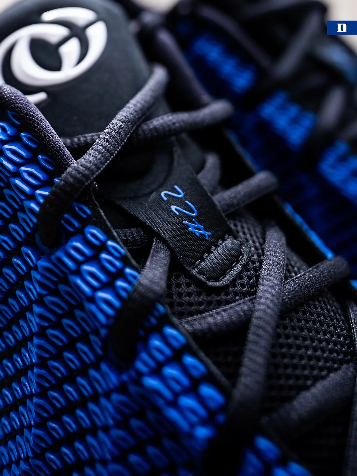 Close detail of lace area, white logo on black tongue, blue #22 tag, blue knit texture, Duke