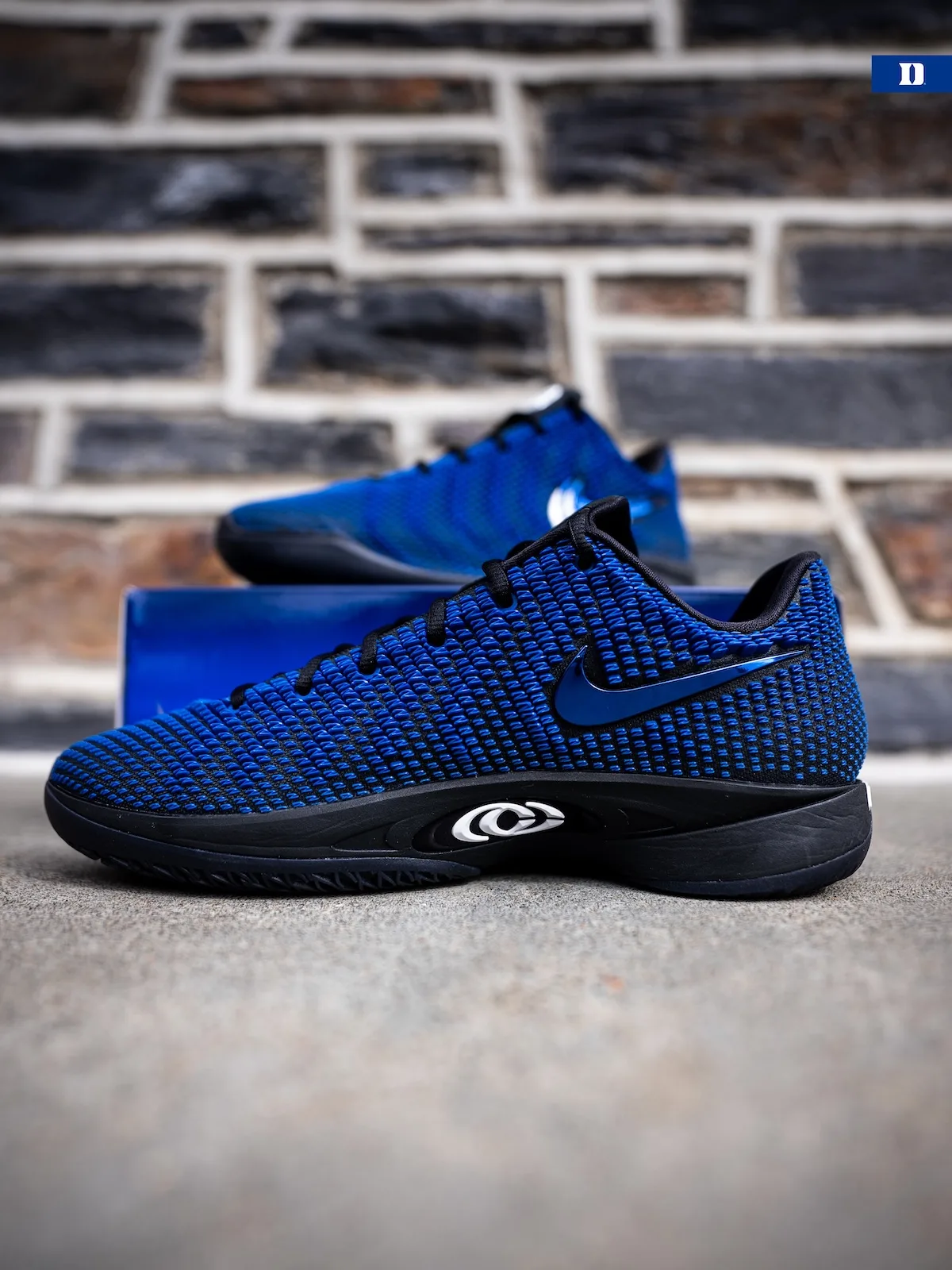 Lateral view on concrete, blue knit, black sole, second shoe on blue box, stone wall, Duke