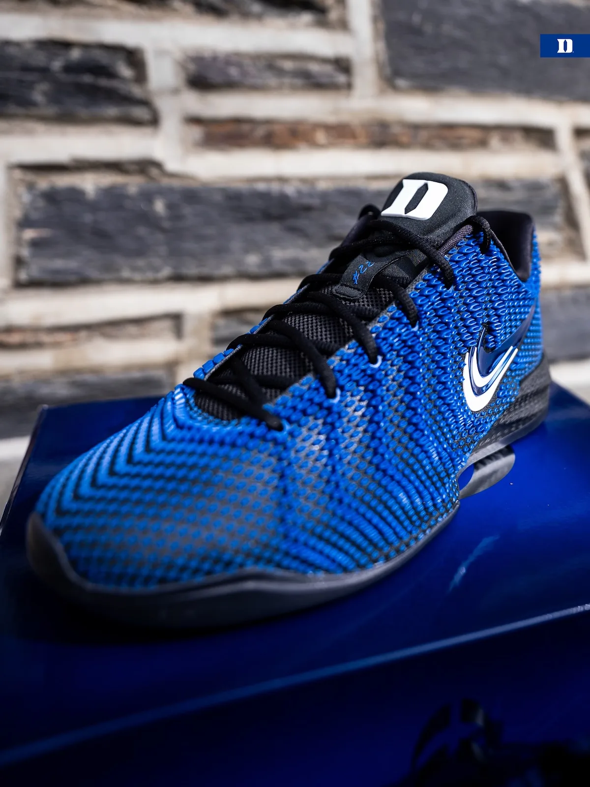 Toe and lateral three-quarter view on blue box, blue knit, white Duke D, stone wall, Duke