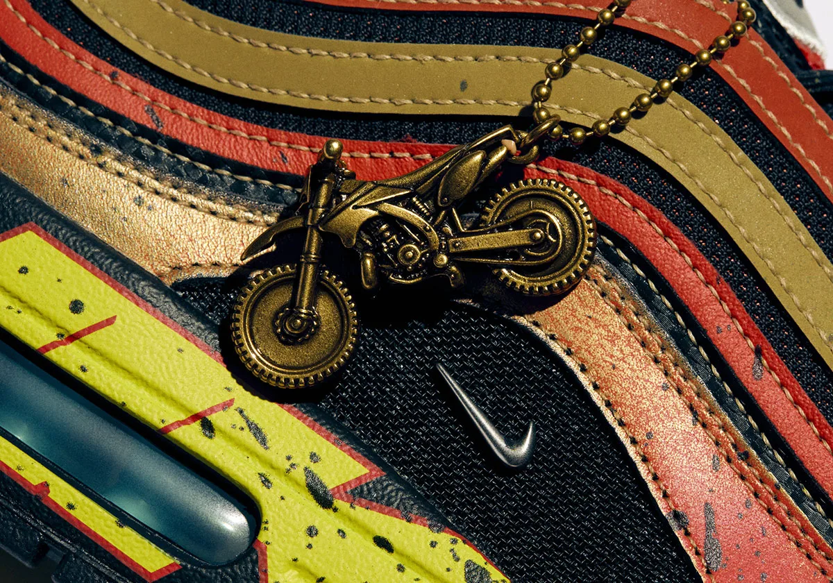 Detail of a gold motorbike charm on a ball chain over red, gold and black striped upper, Freestyle 2027 Collection