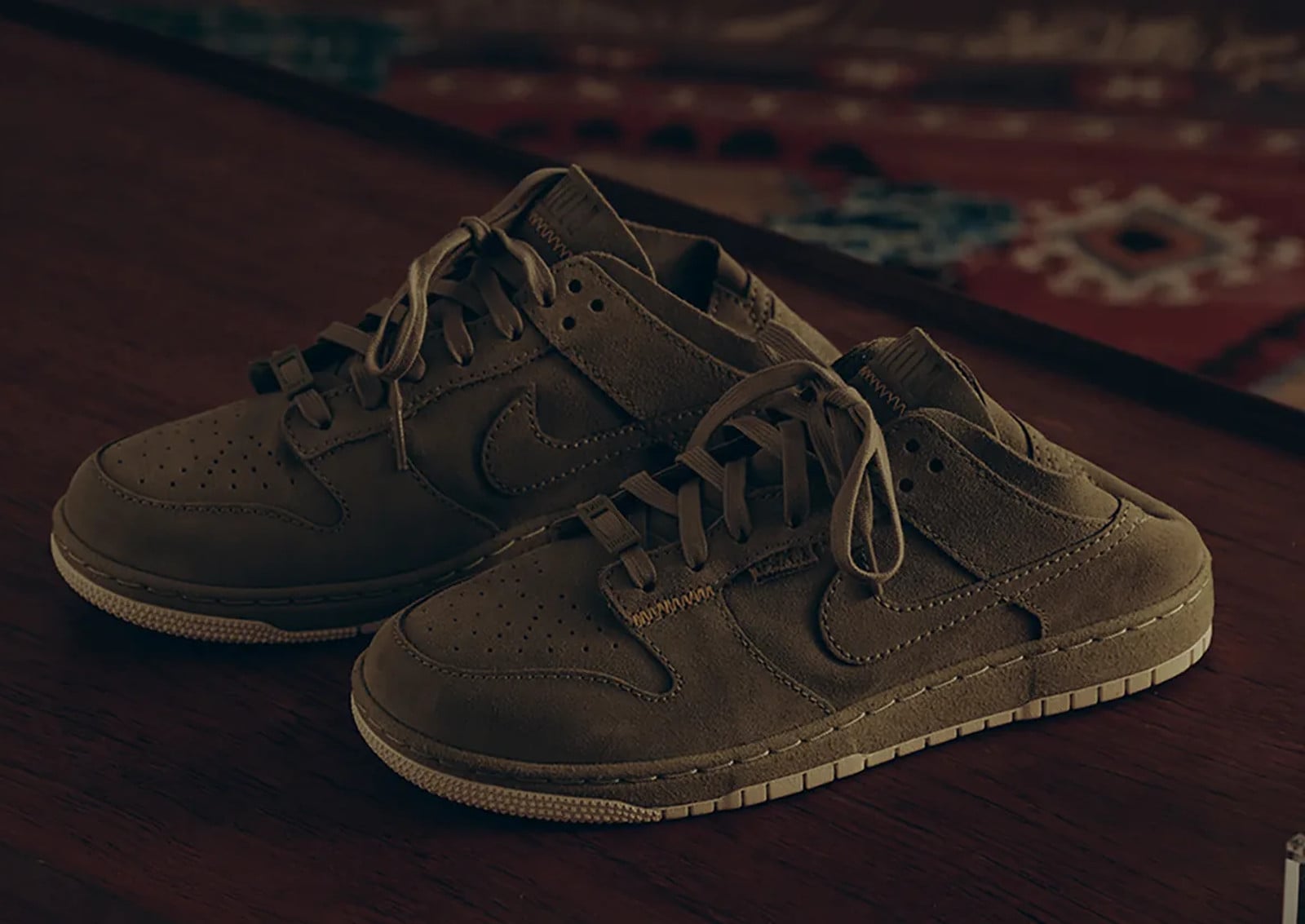 Pair of olive-brown suede low-top mules on a wooden table, patterned rug, Union x Nike Dunk Low “Natural Selection” Pack