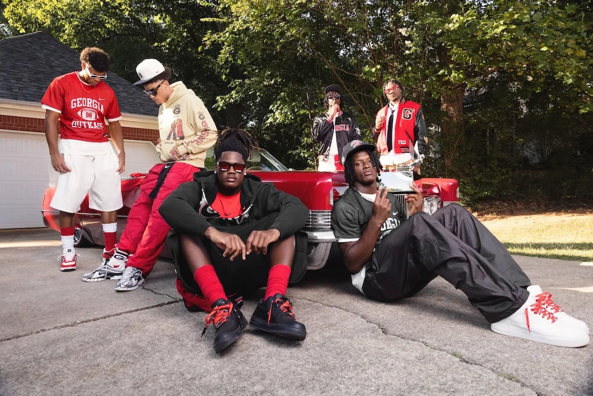 Group posed around a red vintage car on a driveway, black and white sneakers with red laces, Outkast Football Collection