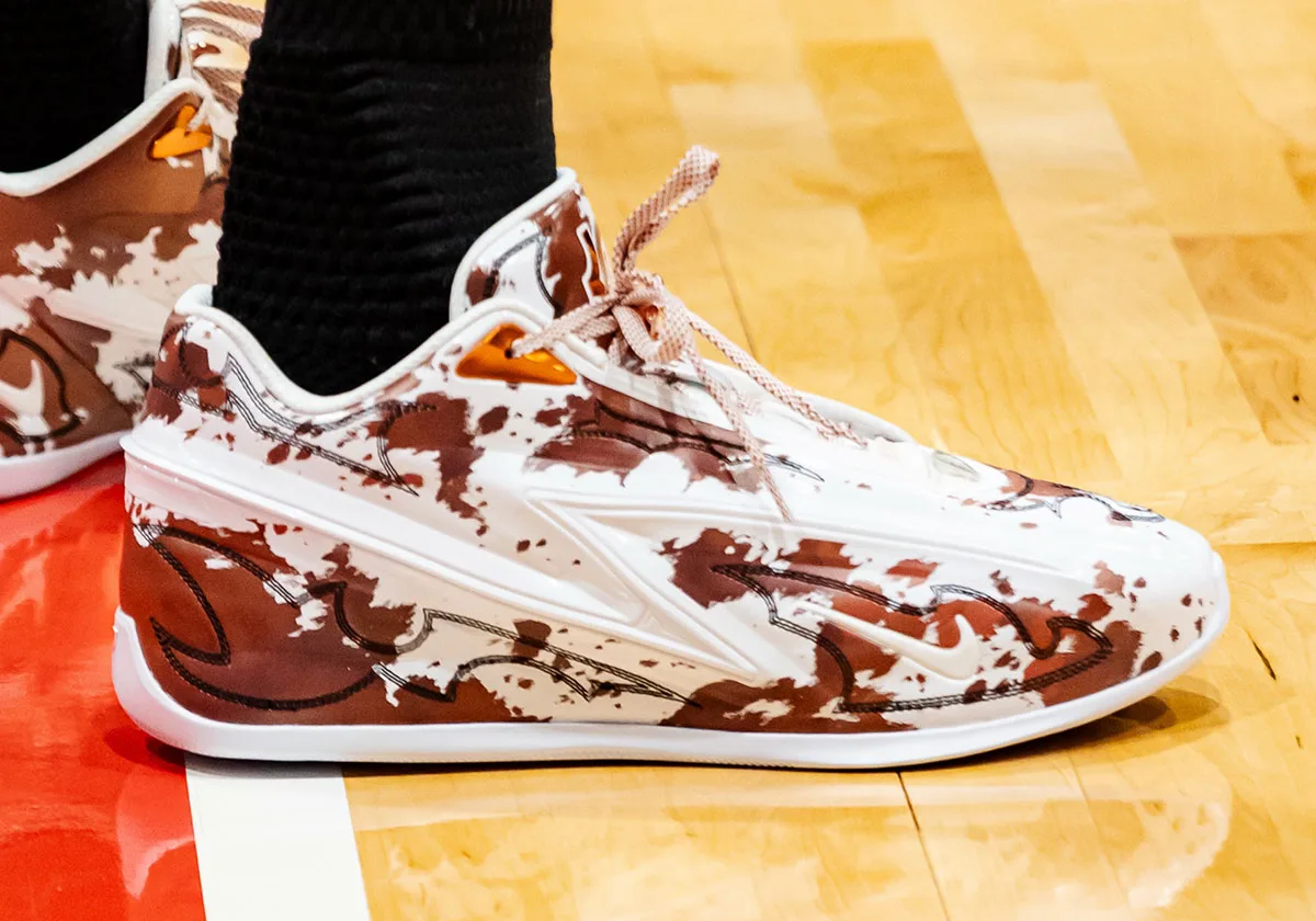 On-foot lateral view, glossy white upper with brown splatter, black stitching and a Nike swoosh, Texas