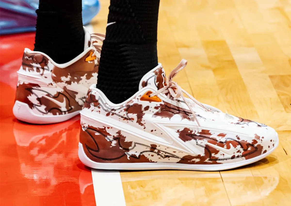 On-foot pair on a court, brown and white splotched upper, black stitched outlines, orange heel pull tab, Texas