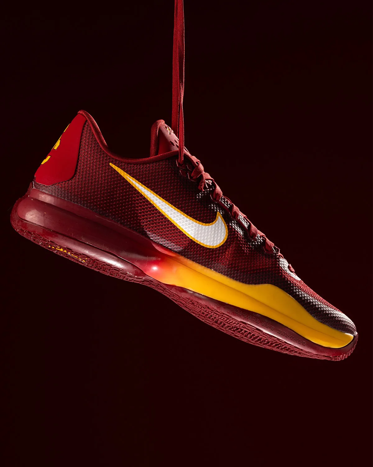 Lateral view of hanging cardinal red shoe with white swoosh and gold midsole, USC