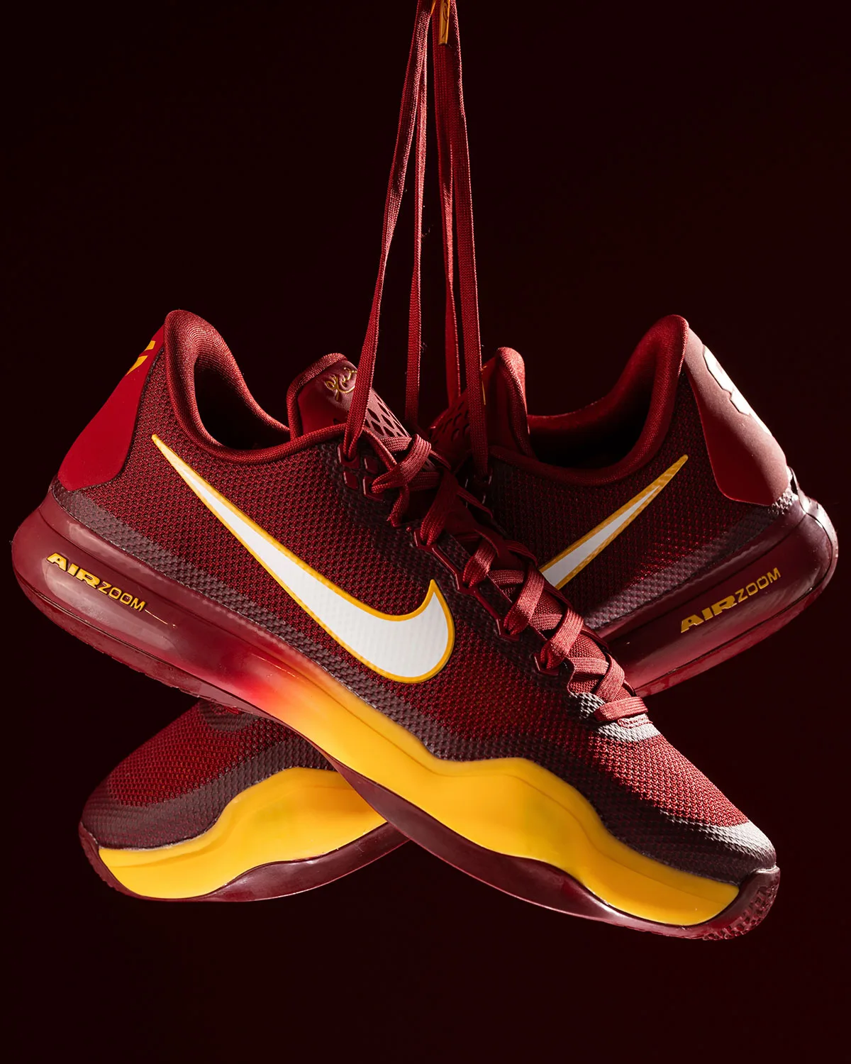 Pair of cardinal red shoes crossed, white swoosh, gold midsole, Air Zoom text, USC