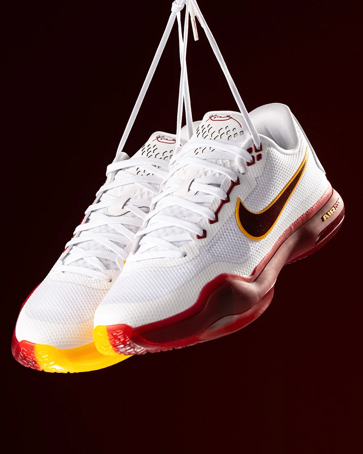 Pair of white shoes hanging by laces, dark red swoosh, red-to-gold sole tip, USC