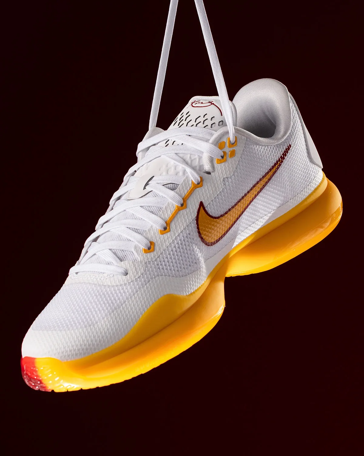 Front three-quarter view of white mesh shoe hanging by laces, gold midsole, gold swoosh, USC