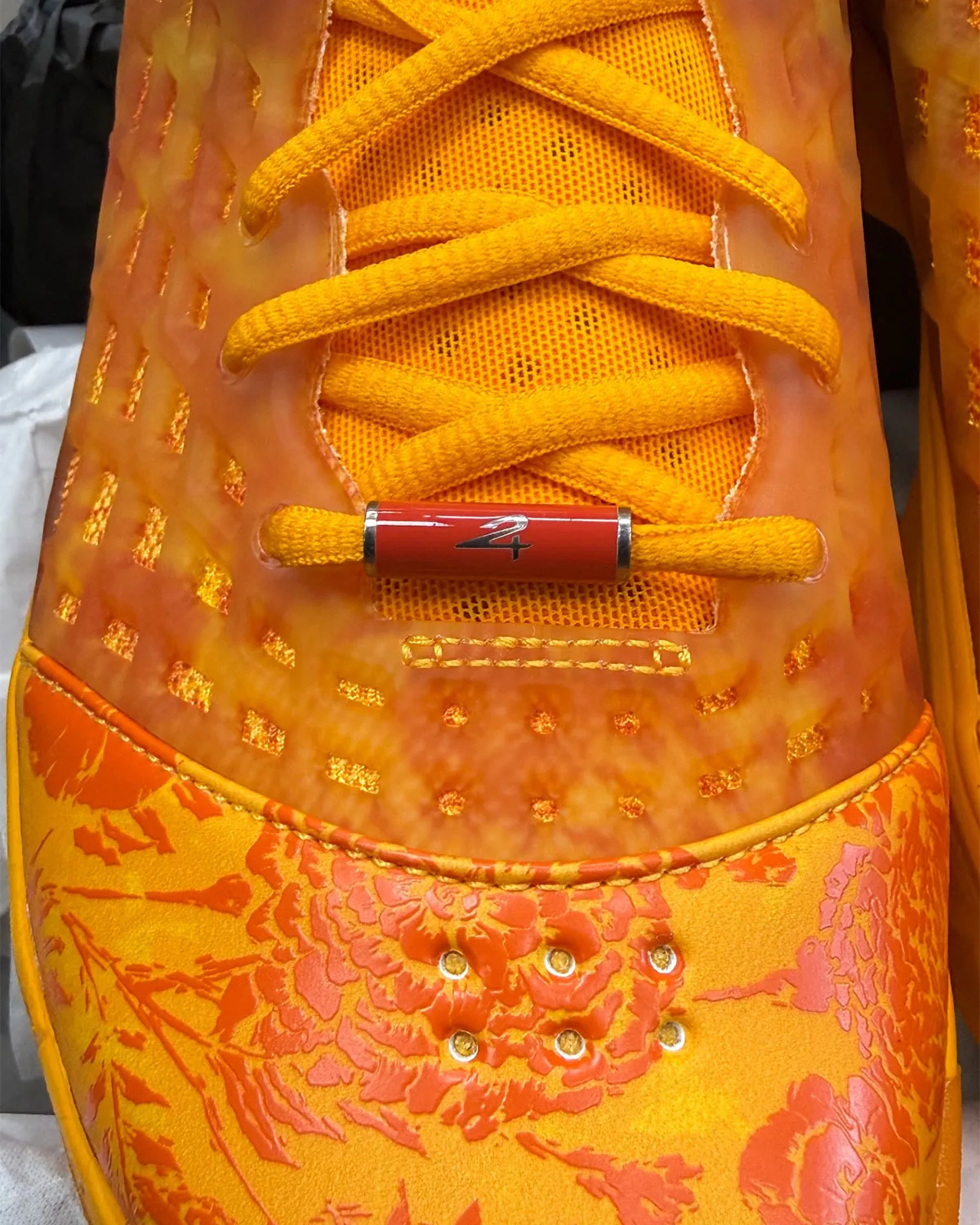 Toe and lace detail: red lace tip with a number 4, orange floral toe cap, gold-ringed vents, Mamba Eterno