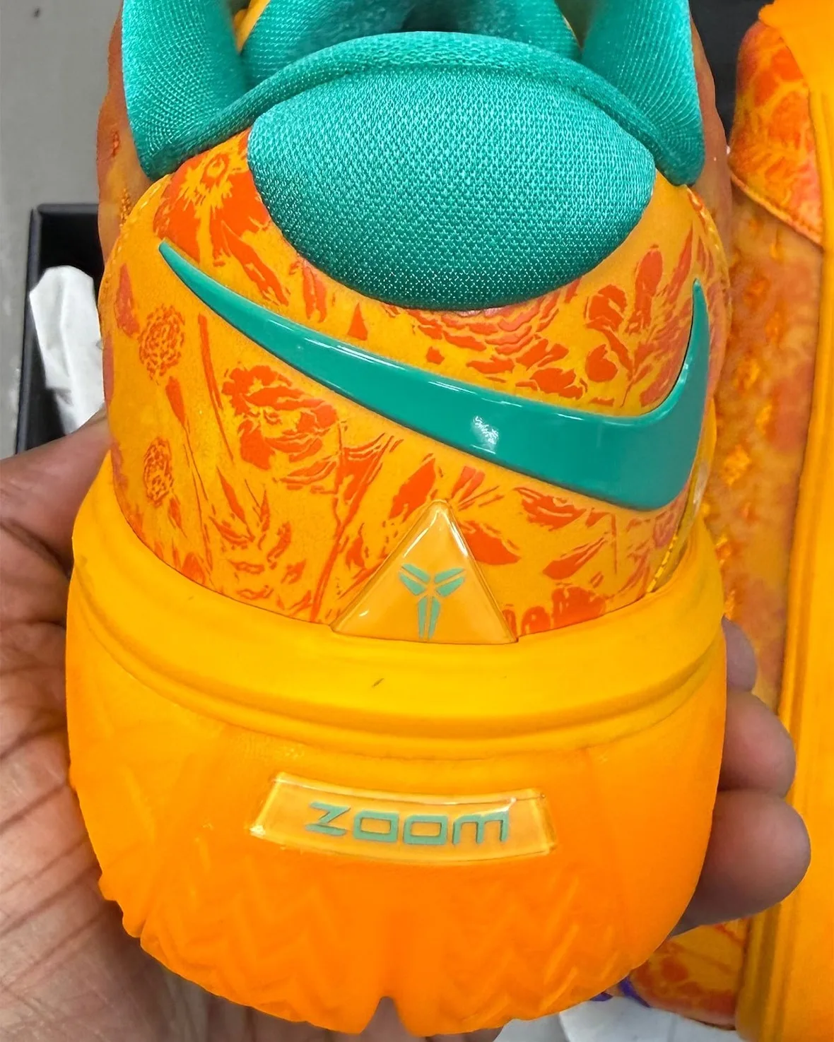 Heel view in hand: teal swoosh and collar, teal Kobe logo, and a Zoom window on orange midsole, Mamba Eterno