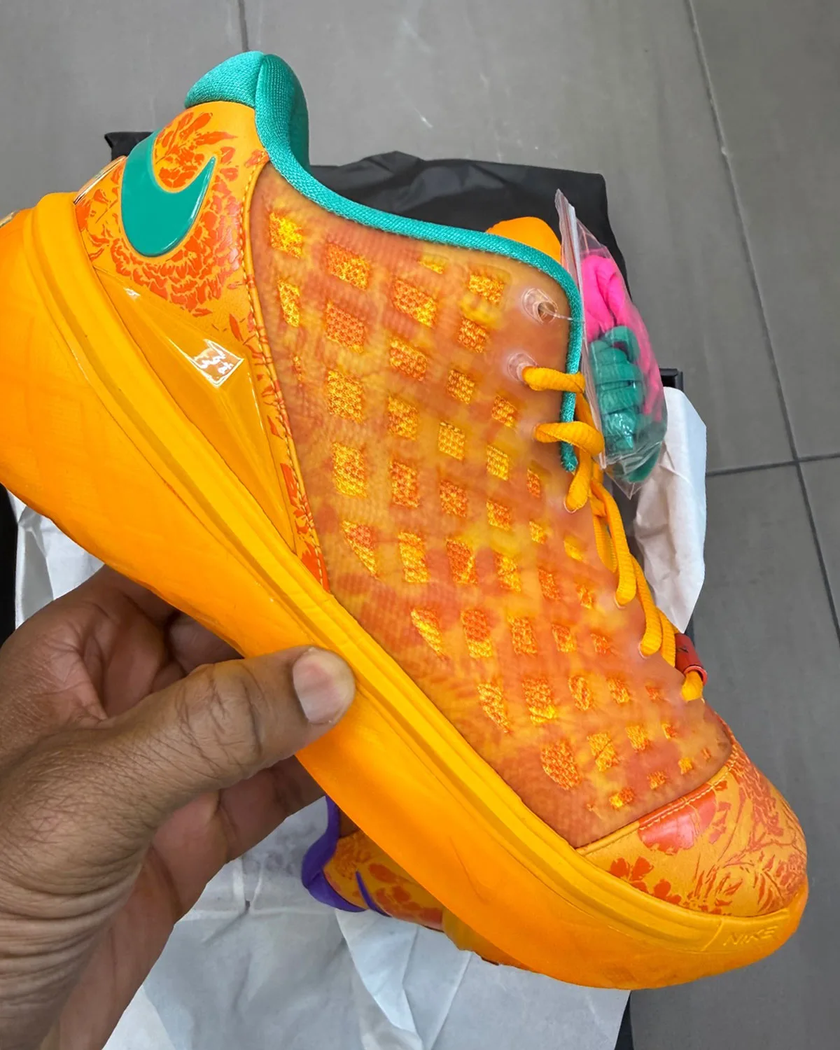 Medial view in hand: orange translucent upper, teal heel swoosh and collar, pink and teal spare laces, Mamba Eterno