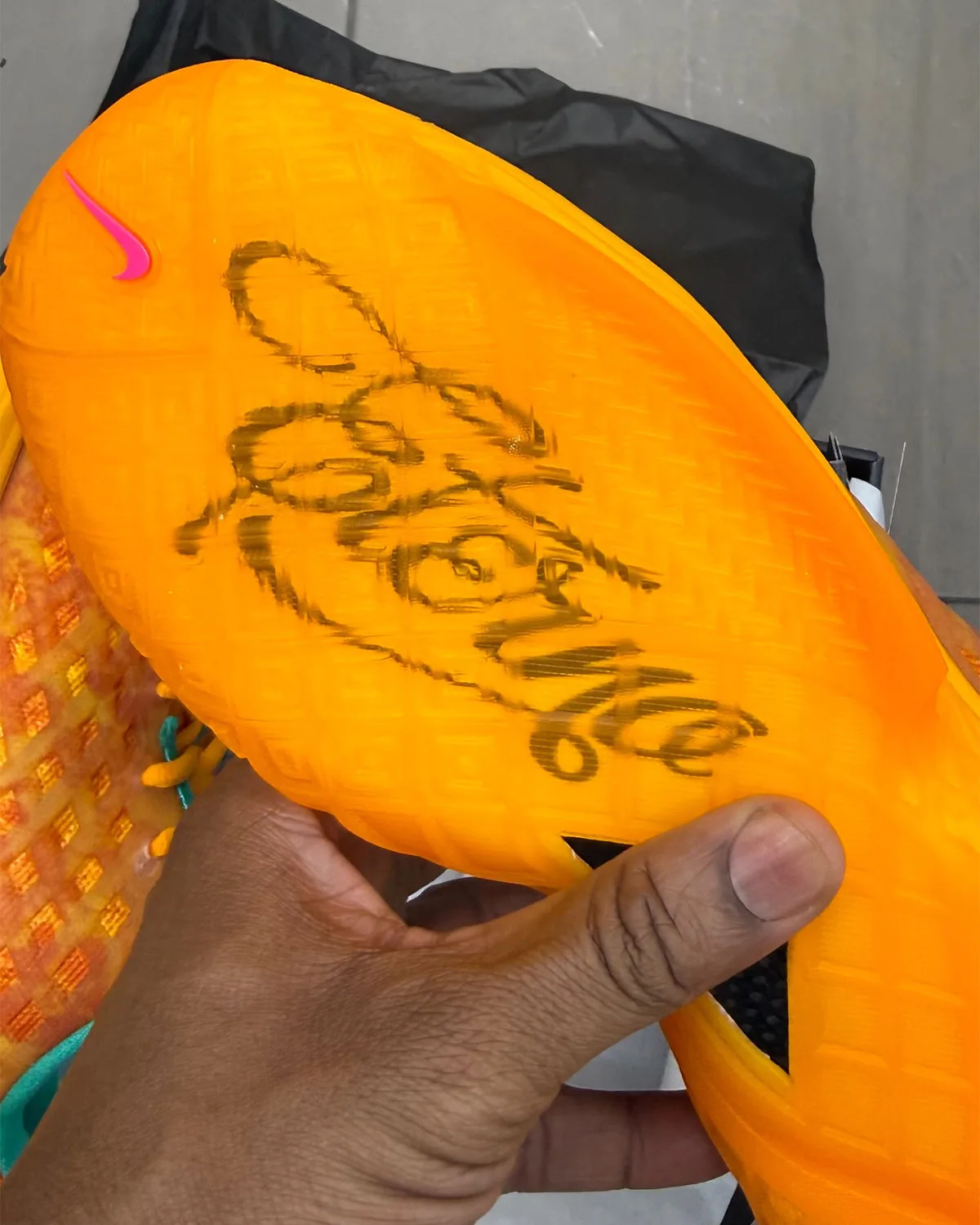 Outsole in hand: orange translucent rubber with a black script signature and a pink swoosh, Mamba Eterno
