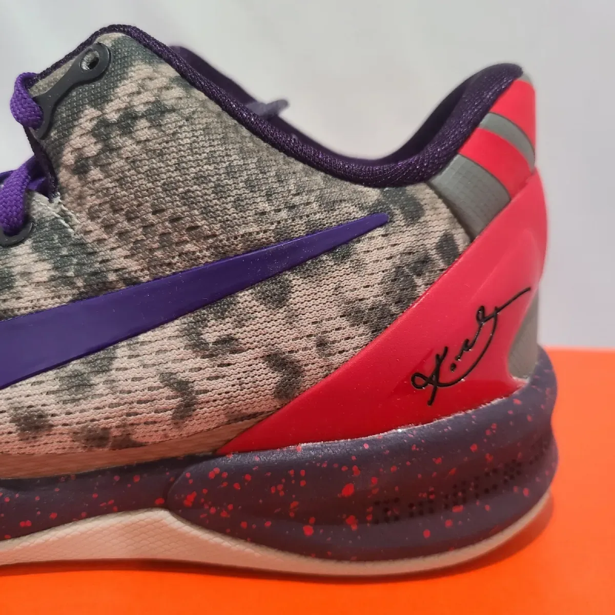 Close-up of lateral heel, purple swoosh, red clip with signature, red-speckled midsole, Mine Grey