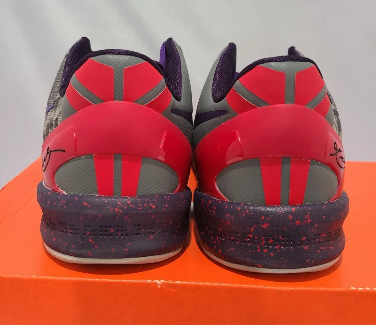 Heel view of pair on an orange shoebox, red heel clips with signature, speckled midsole, Mine Grey