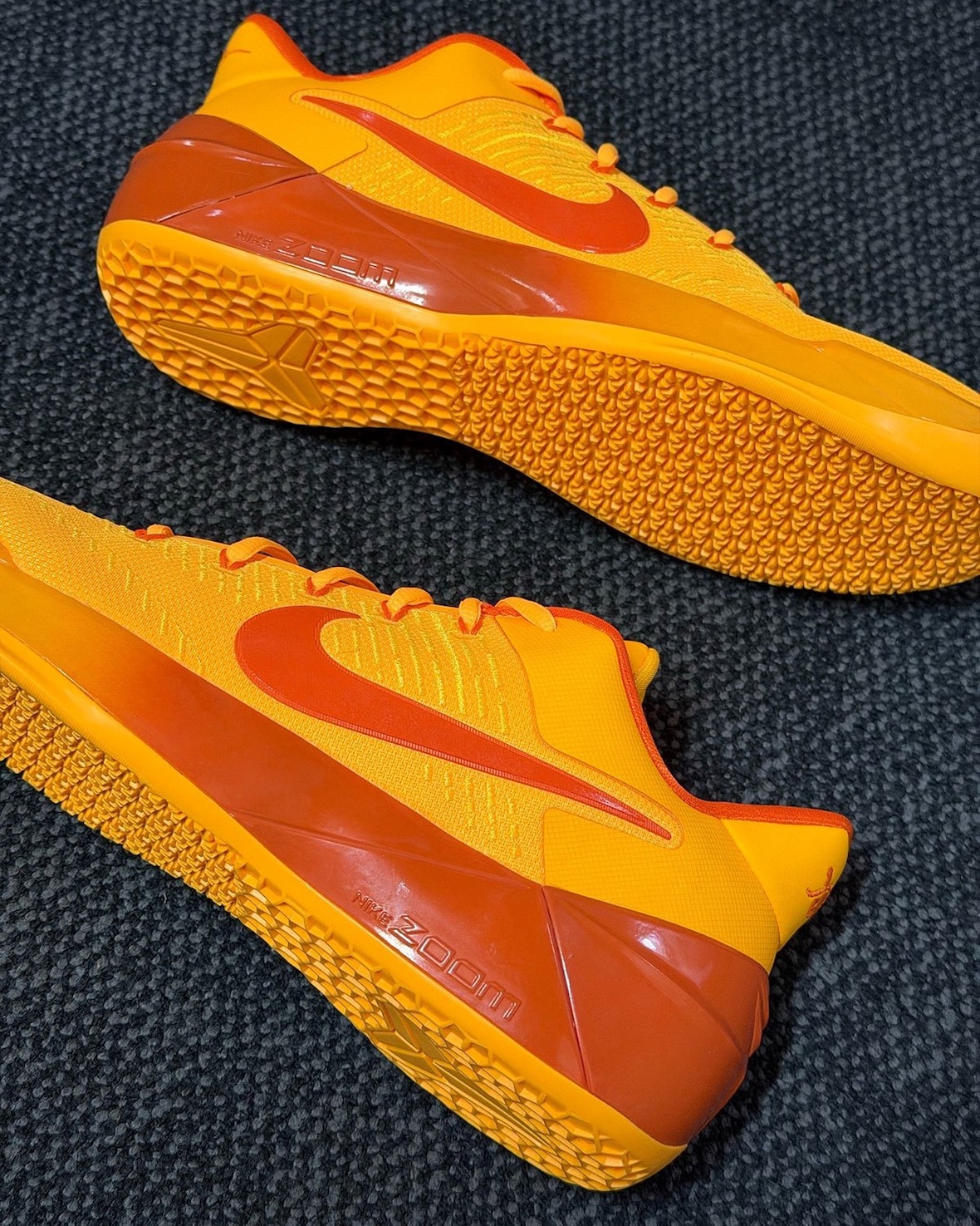 angled rear-to-toe view of both shoes, orange upper with Kobe logo on heel sole, Laser Orange