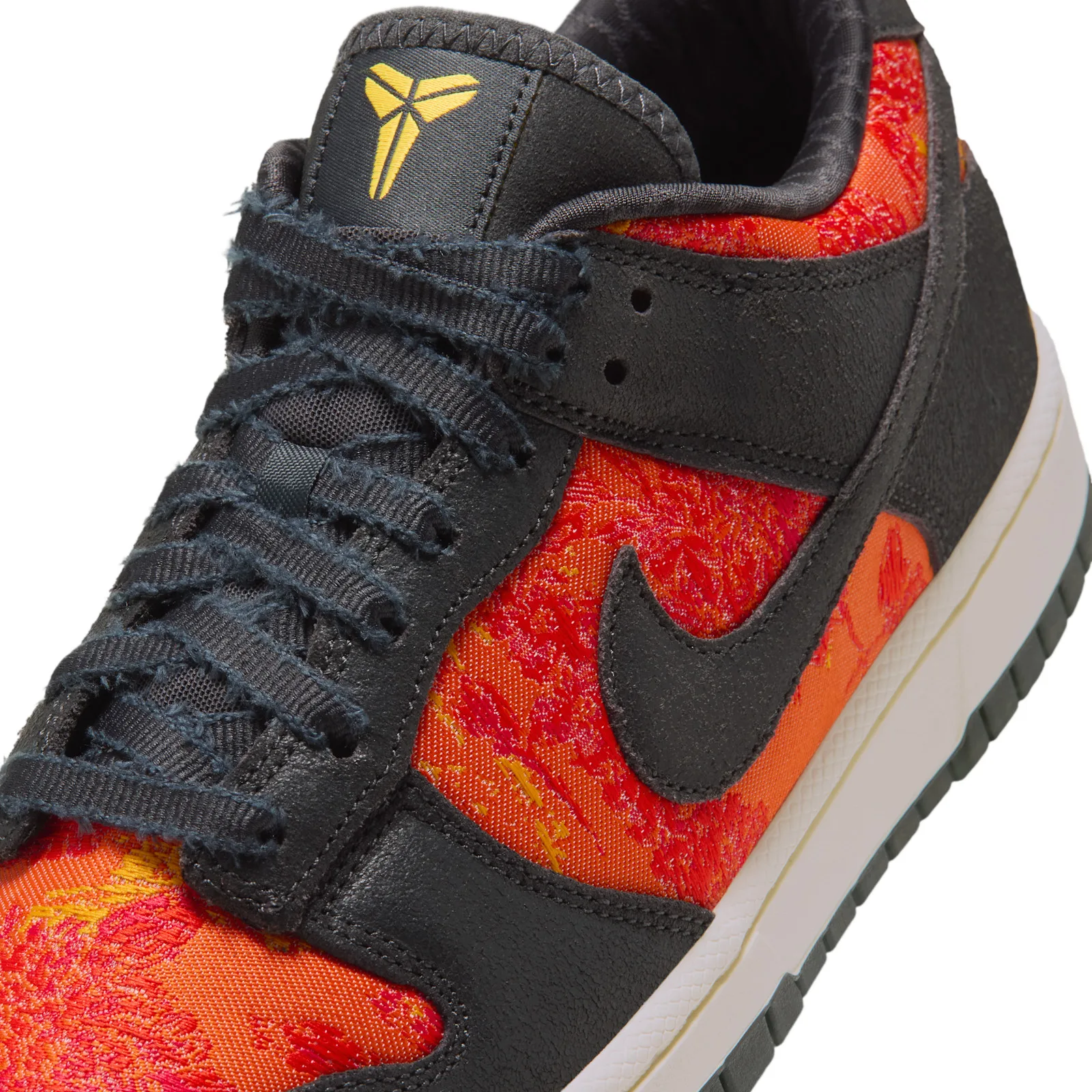 Detail of tongue and laces, yellow logo on black tongue, frayed laces, red-orange jacquard, black swoosh, Mamba Eterno