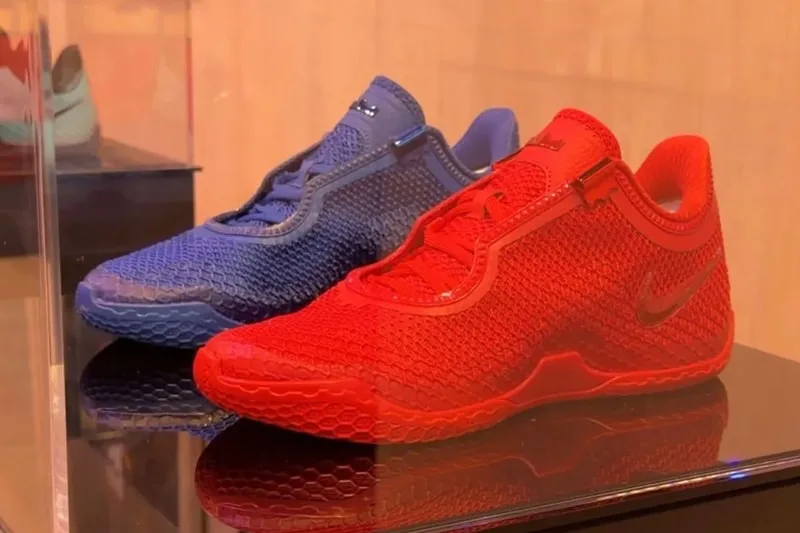 Angled pair view of blue and red knit sneakers with hex-pattern midsoles on glossy case, Philadelphia 76ers Colorways