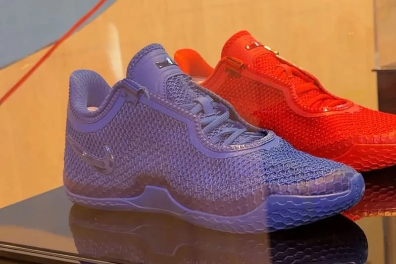 Lateral view of blue mesh sneaker with tonal swoosh, red pair behind on glossy display, Philadelphia 76ers Colorways
