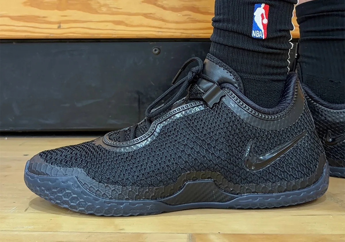 On-foot lateral view on a wood court, black mesh upper, tonal swoosh and black NBA-logo sock, Black