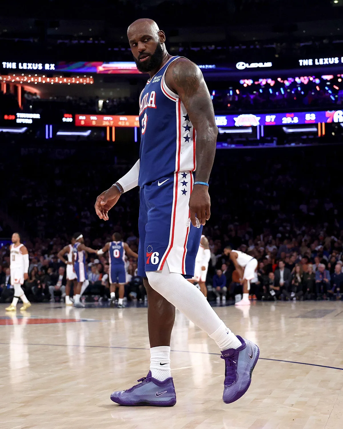 Player in blue Phila jersey standing on court in purple sneakers, Lexus signs and scoreboard behind, Opening Night